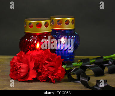 Memory lantern with candles, red carnations and ribbon on wooden table on grey background Stock Photo