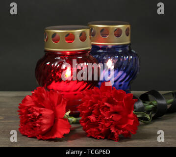 Memory lantern with candles, red carnations and ribbon on wooden table on grey background Stock Photo