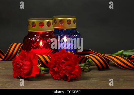 Memory lantern with candles, red carnations and St. George ribbon on wooden table on grey background Stock Photo