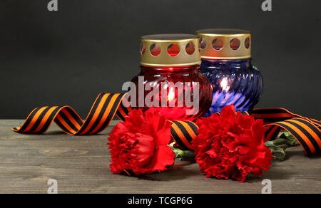 Memory lantern with candles, red carnations and St. George ribbon on wooden table on grey background Stock Photo
