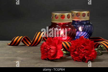 Memory lantern with candles, red carnations and St. George ribbon on wooden table on grey background Stock Photo