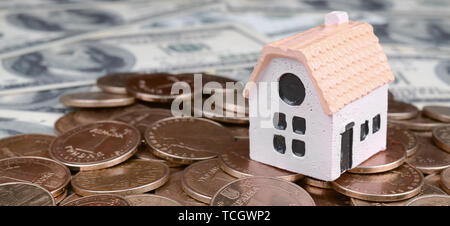 Mini house model on big coins stack on many dollar bills as background. Risk, Assets and Property Investment concept Stock Photo