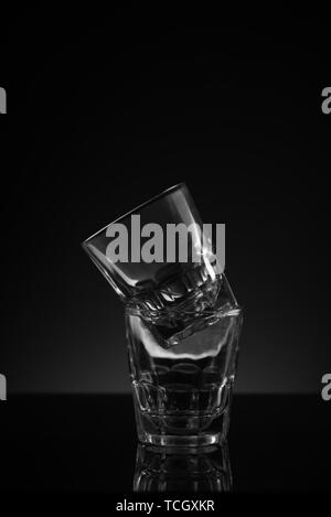 Stacked clear glass shot glasses black background reflective surface and awkward arrangement Stock Photo