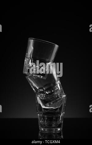 Stacked clear glass shot glasses black background reflective surface and awkward arrangement Stock Photo