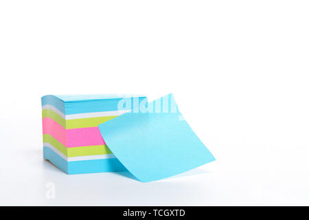 A stack of sticky note paper with one pulled off and ready to be written on. Mostly blue with green and pink isolated on white. Stock Photo