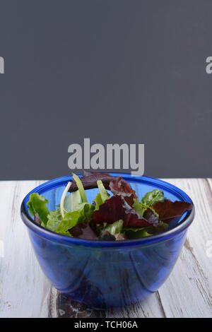 Spring mix salad in a blue glass bowl on a white wood table top and a black chalk board in background. Stock Photo