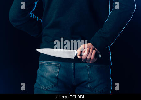 cropped view of murderer hiding knife behind back on black Stock Photo