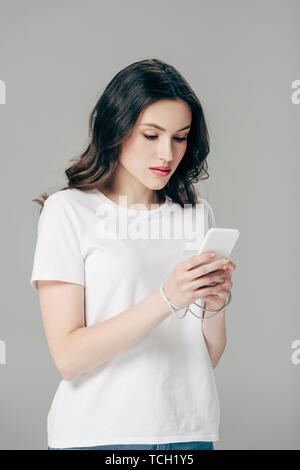 concentrated young girl in white t-shirt using smartphone isolated on grey Stock Photo