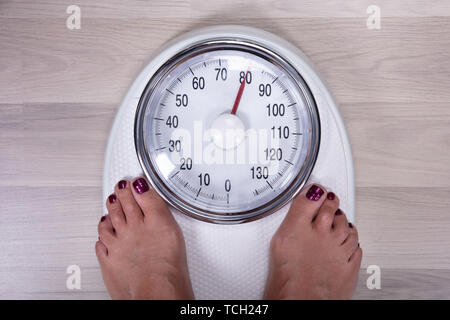 An Overhead View Of Woman's Foot On Weighting Scale Over The Hardwood Floor Stock Photo