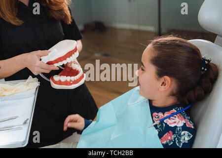 Dentist teaching cute little girl about proper tooth-brushing, using dental jaw model and toothbrush in dental clinic. Dentistry, oral hygiene concept Stock Photo