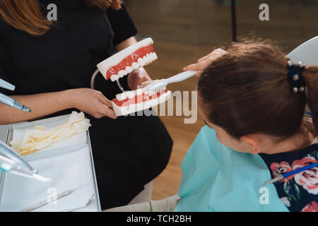 Dentist teaching cute little girl about proper tooth-brushing, using dental jaw model and toothbrush in dental clinic. Dentistry, oral hygiene concept Stock Photo