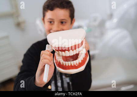 Dentist teaching cute little boy about proper tooth-brushing, using dental jaw model and toothbrush in dental clinic. Dentistry, oral hygiene concept. Stock Photo