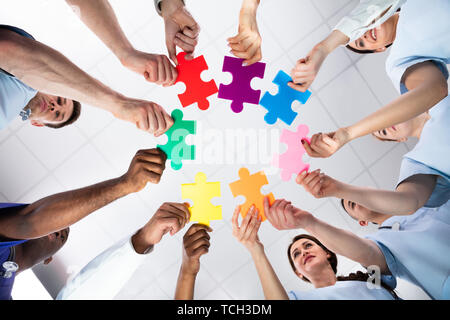 Low Angle View Of Young Diverse Medical Team Solving Colorful Jigsaw Puzzle At Hospital