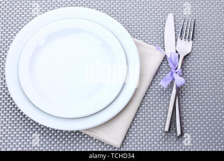 White empty plates with fork and knife tied with a ribbon on a grey tablecloth Stock Photo