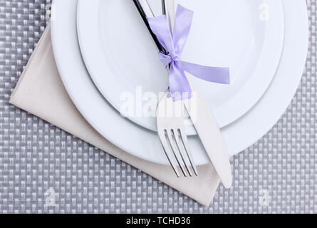 White empty plates with fork and knife tied with a ribbon on a grey tablecloth Stock Photo