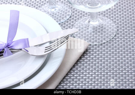 White empty plates, fork and knife tied with a ribbon and glasses on a grey tablecloth Stock Photo
