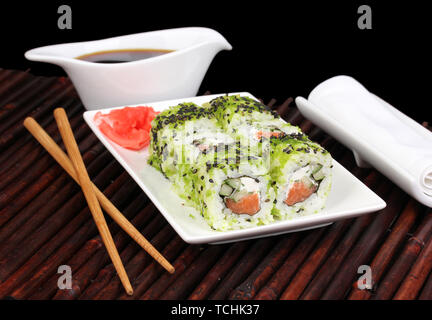 Tasty rolls served on white plate with chopsticks on bamboo mat on black background Stock Photo