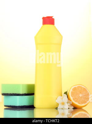 Dishwashing liquid with sponges and lemon with flowers on yellow background Stock Photo