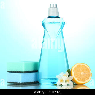 Dishwashing liquid with sponges and lemon with flowers on blue background Stock Photo