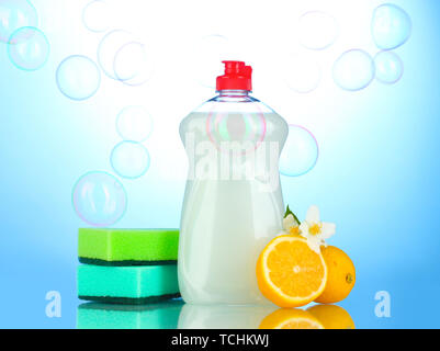 Dishwashing liquid with sponges and lemon with flowers on blue background Stock Photo