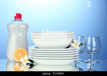 empty clean plates and glasses with dishwashing liquid and lemon on blue background Stock Photo