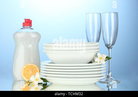 empty clean plates and glasses with dishwashing liquid and lemon on blue background Stock Photo