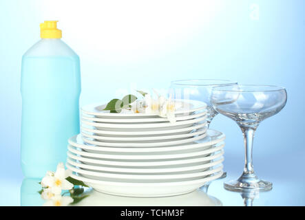 empty clean plates and glasses with dishwashing liquid on blue background Stock Photo