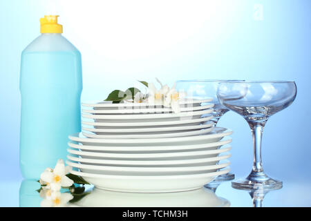 empty clean plates and glasses with dishwashing liquid on blue background Stock Photo