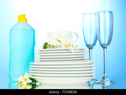 empty clean plates and glasses with dishwashing liquid on blue background Stock Photo