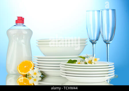 empty clean plates and glasses with dishwashing liquid and lemon on blue background Stock Photo