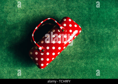 Case for glasses in the form of a women's handbag red with white polka dots on a green background. View from above. Flat lay Stock Photo