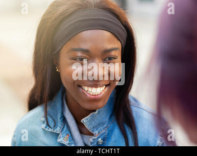 Two friends, of African and Caucasian ethnicity, talk sitting on a bench outdoors. Stock Photo