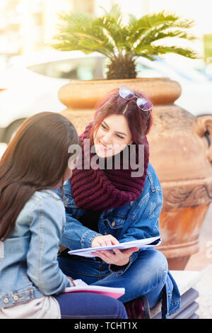 Two young women, of African and Caucasian ethnicity, study outdoors sitting on a bench. Stock Photo