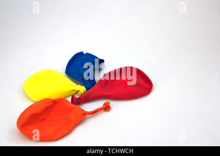 Four used, deflated and broken balloons of red, blue, orange and yellow colors on a white table Stock Photo