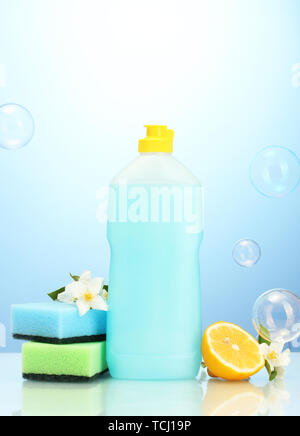 Dishwashing liquid with sponges and lemon with flowers on blue background Stock Photo