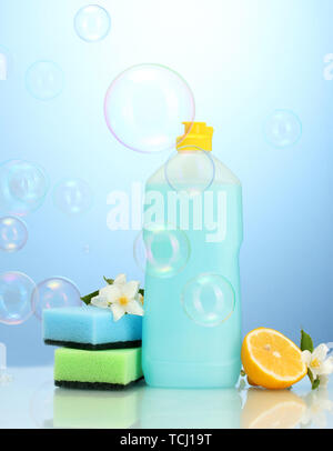 Dishwashing liquid with sponges and lemon with flowers on blue background Stock Photo