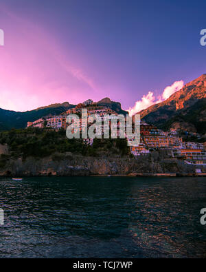 Positano coast as seen from the water showing a pink sky and mountain looming in the background Stock Photo
