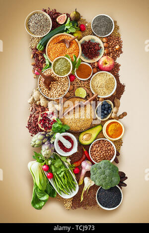 Multiple bowls of different kinds of rice and several types of beans sitting on bed of herbs on red surface Stock Photo