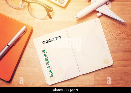travel checklist concept. notebook with blank checklist on wooden background with glasses and plane model Stock Photo