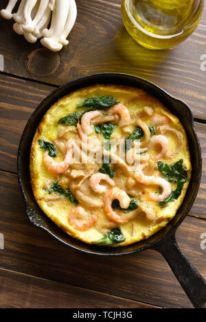 Mushroom and spinach frittata with shrimps in frying pan on wooden background. Top view, flat lay Stock Photo