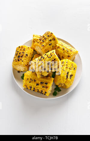 Grilled corn cobs on plate over white stone background with copy space. Tasty vegetarian vegan food. Stock Photo