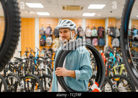 Man in cycling helmet holds bicycle tyre, shopping Stock Photo