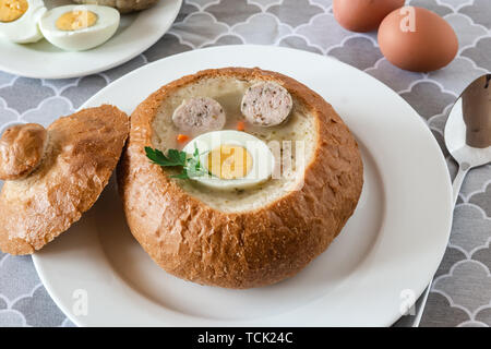 The sour soup (zurek) made of rye flour with sausage and egg served in bread bowl. Traditional polish sour rye soup, popular Easter dish. Stock Photo