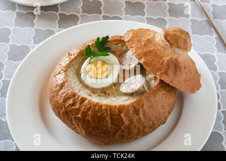 The sour soup (zurek) made of rye flour with sausage and egg served in bread bowl. Traditional polish sour rye soup, popular Easter dish. Stock Photo