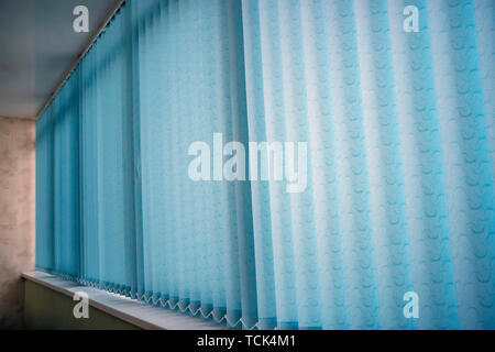 Blue vertical blinds on the long window on the balcony. Modern interior design. Closed window from sunlight Stock Photo