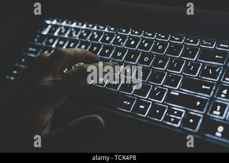 Programmer or computer hacker typing code on laptop keyboard. The keypad is lit in white light. hand presses a key on your computer Stock Photo