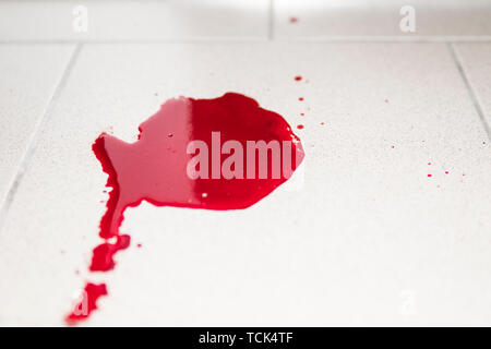 Conceptual image with blood on it resting on tiles on the floor. A puddle of dried blood on the tiled bathroom floor. Stock Photo