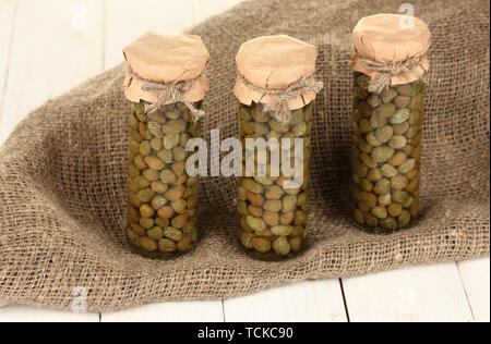 Glass jars with tinned capers in sack on white wooden background Stock Photo