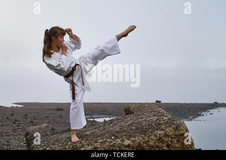 Young Woman in Kimono practicing karate, Japanese martial arts on river coast. Early foggy morning Stock Photo