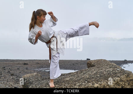 Young Woman in Kimono practicing karate, Japanese martial arts on river coast. Early foggy morning Stock Photo